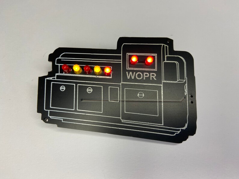 May include: A black WOPR computer system replica with a series of red and yellow lights on the top. The lights are lit up and the text "WOPR" is visible on the front of the system.