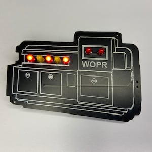 May include: A black WOPR computer system replica with red and yellow lights. The system has a control panel with a series of buttons and a display screen.