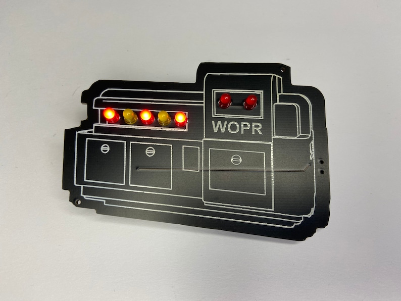 May include: A black WOPR computer system replica with red and yellow lights. The system has a control panel with a series of buttons and a display screen.
