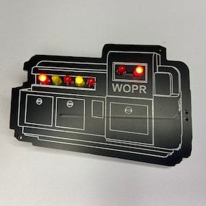 May include: A black WOPR computer panel with a series of red and yellow lights. The panel has a white outline and the text "WOPR" is printed in white.