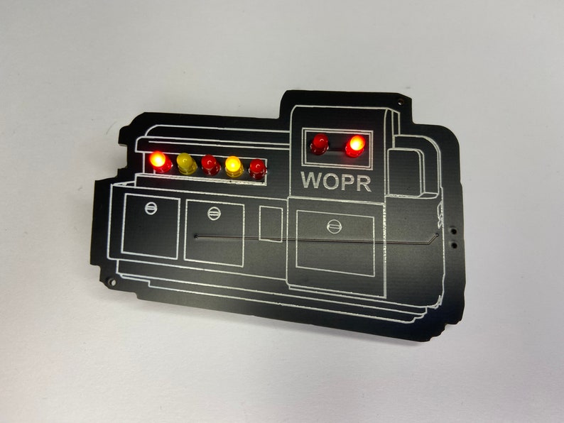 May include: A black WOPR computer panel with a series of red and yellow lights. The panel has a white outline and the text "WOPR" is printed in white.