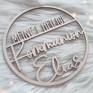 Könnte beinhalten: Ein Holz-Kreis mit dem Text "Meine 1. Heilige Kommunion Elias" in einer kursivschrift.