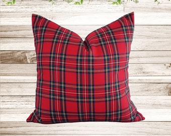 Könnte beinhalten: Quadratisches rotes Plaid-Kissen mit einem klassischen Muster aus schwarzen, marineblauen und gelben Linien. Das Kissen ist ein dekoratives Element, perfekt, um jedem Raum einen Hauch von Farbe und Muster zu verleihen. Auf hellem Holzgrund.