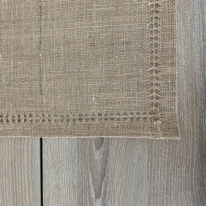 May include: A close-up of a brown hessian fabric with a woven edge. The fabric is textured and has a natural, rustic look.