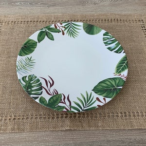 May include: A white ceramic dinner plate with a green and red tropical leaf design. The plate is 35 to 45 cm in diameter and is sitting on a brown hessian placemat.