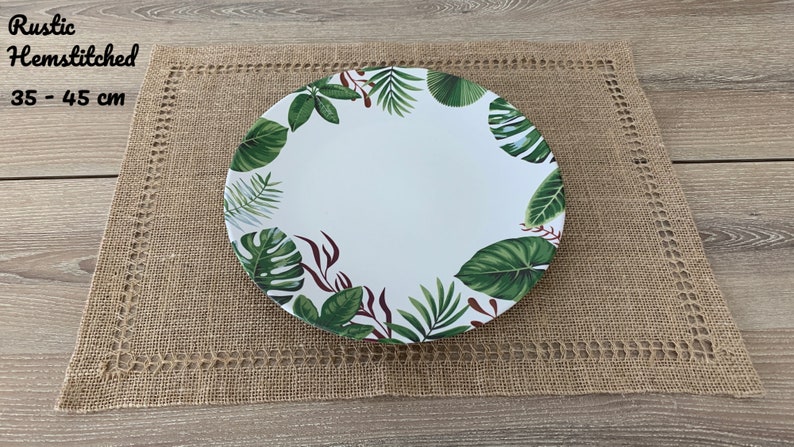 May include: A white ceramic dinner plate with a green and red tropical leaf design. The plate is 35 to 45 cm in diameter and is sitting on a brown hessian placemat.