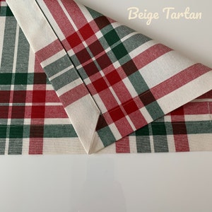 May include: Beige tartan fabric with red, green, and brown plaid pattern. The fabric is folded in half, showing the seam.