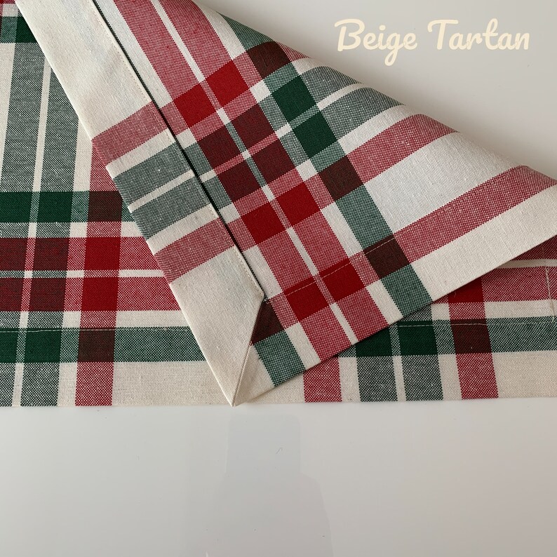 May include: Beige tartan fabric with red, green, and brown plaid pattern. The fabric is folded in half, showing the seam.