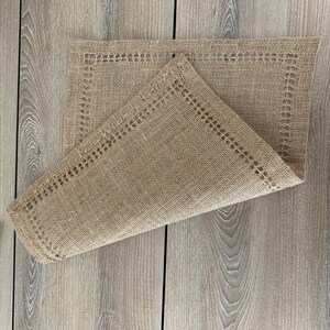 May include: A brown burlap placemat with a decorative lace border. The placemat is folded in half and has a rustic, natural look.