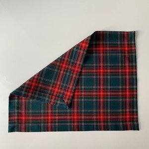 May include: A red and green plaid fabric placemat with a folded corner. The placemat is made of a woven fabric with a checkered pattern.
