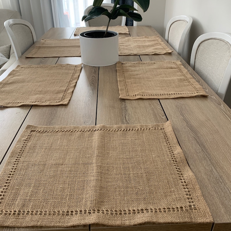 May include: A set of six brown woven placemats with a decorative stitched border. The placemats are arranged on a light brown wooden table.