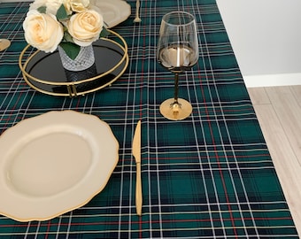 May include: A green and white plaid tablecloth with a gold rimmed plate, a gold knife, and a gold wine glass on top. A bouquet of white flowers in a clear glass vase sits on a black and gold tray.