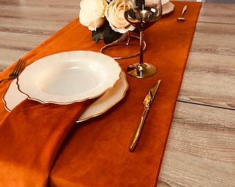 May include: A close-up of a table setting with a brown velvet table runner, white plates with gold trim, gold cutlery, and a gold wine glass. A bouquet of white roses is in the centre of the table.