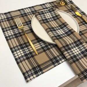 May include: A brown and black plaid placemat with a white plate and gold fork on top. The placemat is made of woven fabric and has a subtle sheen.