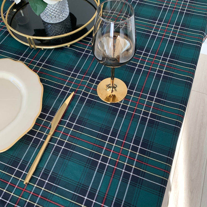 May include: A green, black, red and white tartan tablecloth with a gold knife, a white plate and a gold-rimmed wine glass on top.