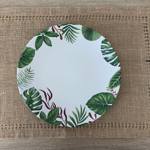 May include: A white ceramic dinner plate with a green and brown tropical leaf design. The plate is on a brown woven placemat.