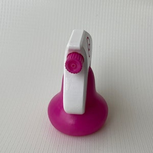 Puede incluir: Una botella de spray de pl&aacute;stico rosa con un gatillo blanco y una perilla rosa. La botella tiene una base redonda y una etiqueta blanca con un c&iacute;rculo rosa.
