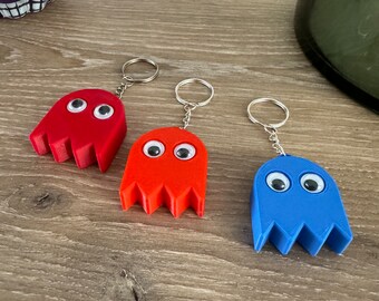 May include: Three Pac-Man ghost keychains, one red, one orange, and one blue. Each keychain has googly eyes and a silver key ring.
