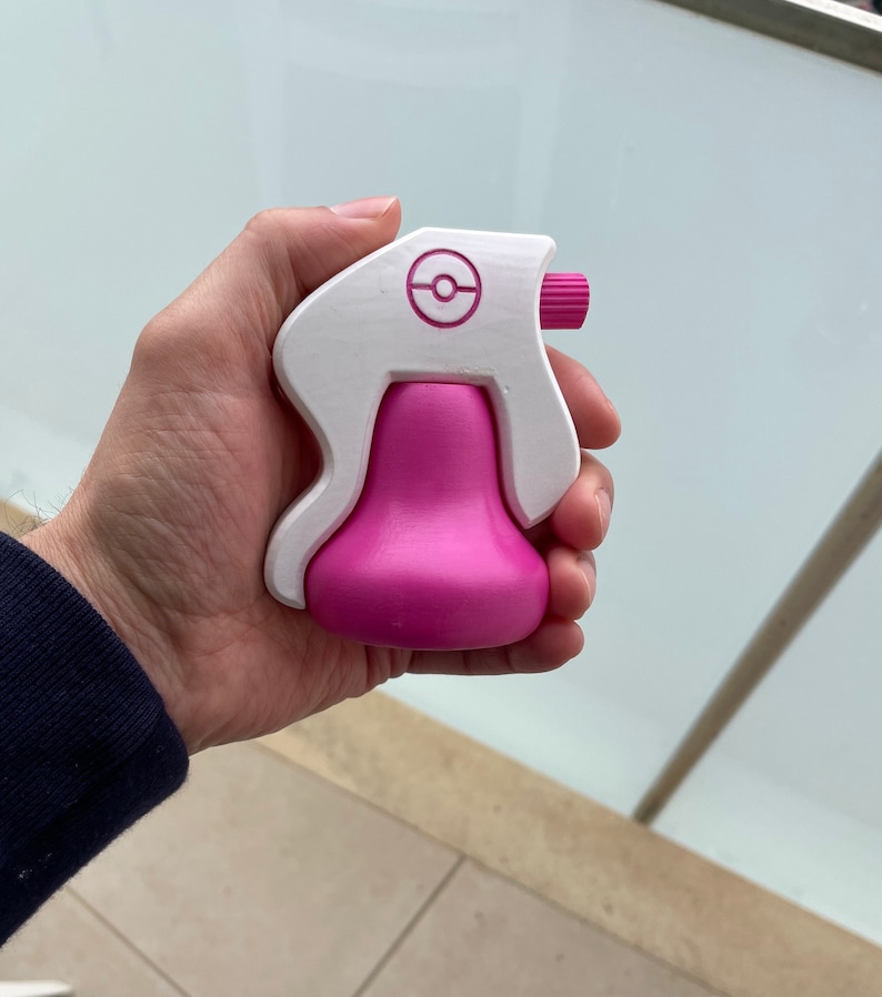 Puede incluir: Una botella de spray de pl&aacute;stico blanca y rosa con un logotipo de Pokeball en el lateral. La botella est&aacute; dise&ntilde;ada para parecerse a un personaje de Pokemon.