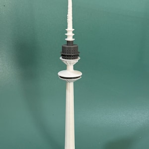 May include: A white 3D printed model of a tower with a gray top and a circular base.