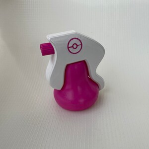 Puede incluir: Una botella de spray de pl&aacute;stico rosa y blanco con un logotipo de Pokeball en el lateral. La botella est&aacute; dise&ntilde;ada para parecerse a un personaje de Pokemon.