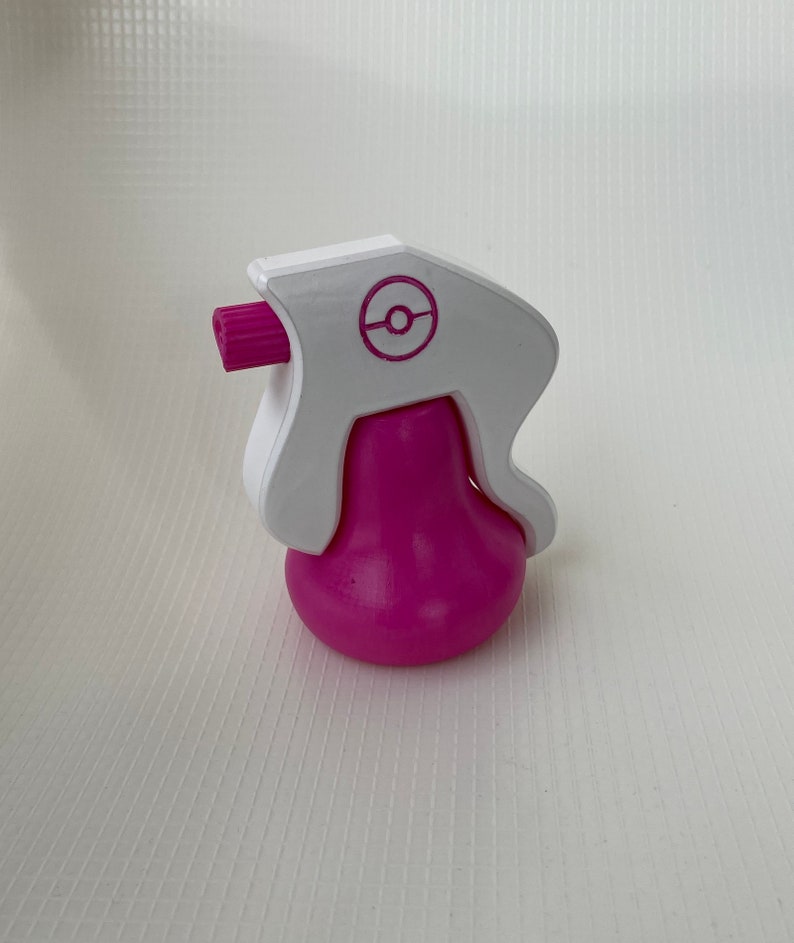 Puede incluir: Una botella de spray de pl&aacute;stico rosa y blanco con un logotipo de Pokeball en el lateral. La botella est&aacute; dise&ntilde;ada para parecerse a un personaje de Pokemon.