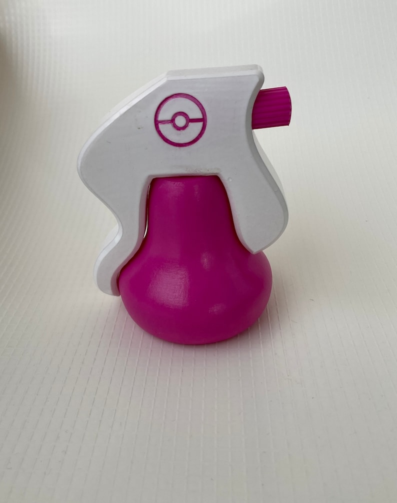 Puede incluir: Una botella de spray de pl&aacute;stico rosa y blanco con un logotipo de Pokeball blanco en la parte superior.