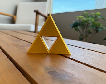 May include: A yellow triangular-shaped object with a smaller triangle cut out of the center. The object is made of plastic and is sitting on a wooden surface.