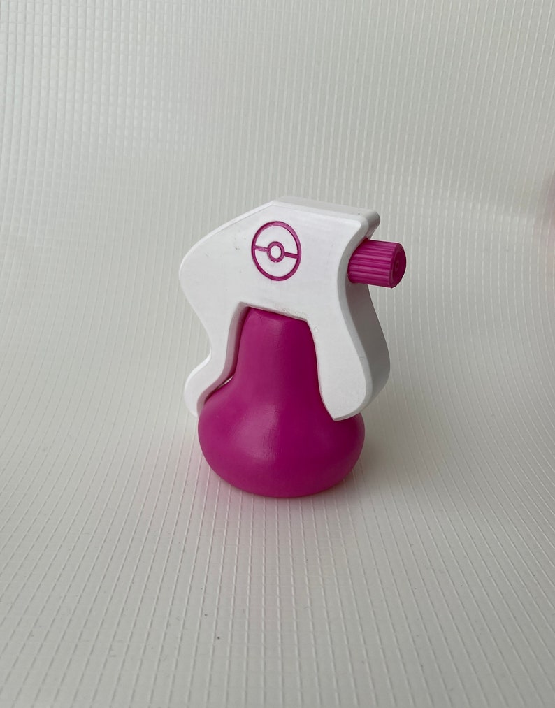 Puede incluir: Botella de spray de pl&aacute;stico blanco con una base rosa y un logotipo de Pokeball rosa en el lateral.