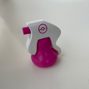 Puede incluir: Una botella de spray de pl&aacute;stico blanca y rosa con un logotipo de Pokeball en la parte superior.