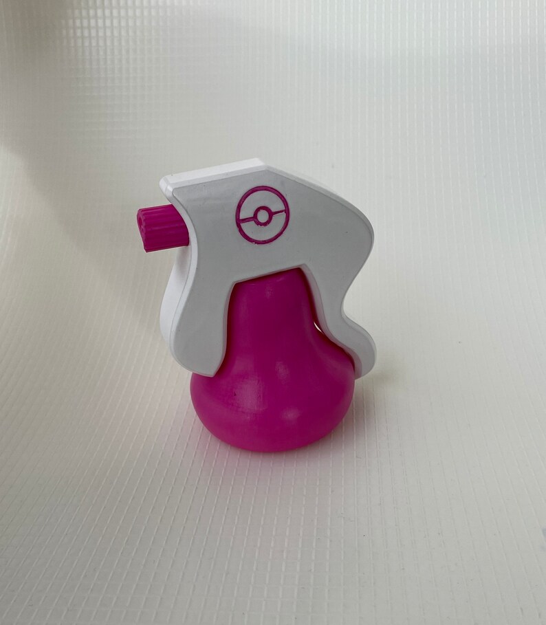 Puede incluir: Una botella de spray de pl&aacute;stico blanca y rosa con un logotipo de Pokeball en la parte superior.