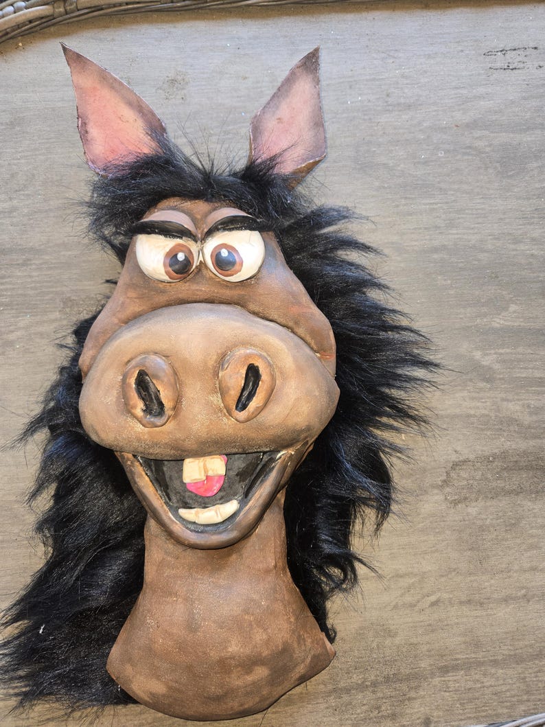 May include: A whimsical donkey mask with a brown face, large expressive eyes, and a wide, toothy grin. The mask features black faux fur around the face and ears, and is likely made of a sturdy material.