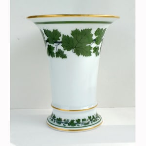 以下が含まれることがあります： 白いセラミック花瓶、フレアトップと金色の縁。 花瓶は上部と基部に緑の葉の模様があります。 花瓶の高さは約20cmです。