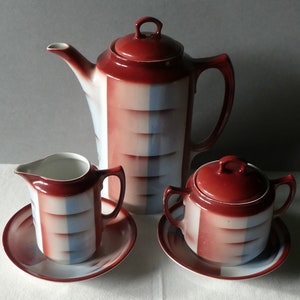 Könnte beinhalten: Ein Vintage-Tee-Set mit einem geometrischen Design in Rot, Weiß und Blau. Das Set enthält eine Teekanne, eine Milchkännchen, eine Zuckerdose und zwei Untertassen.