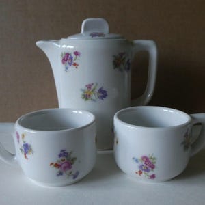 Könnte beinhalten: Ein weißes Porzellan-Tee-Set mit floralem Muster. Das Set enthält eine Teekanne und zwei Tassen.