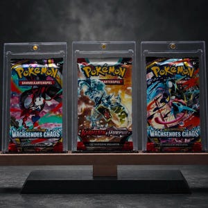 Può includere: Tre bustine di carte collezionabili Pokémon sigillate, esposte in custodie acriliche trasparenti individuali su un supporto in legno. Le confezioni presentano illustrazioni colorate e il testo Pokémon Sammelkartenspiel, Wachsendes Chaos e Karmesin & Purpur.