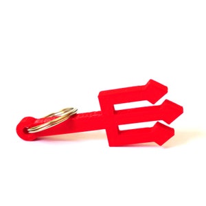 Puede incluir: Un llavero de plástico rojo con forma de tridente. El llavero tiene un anillo de metal dorado.