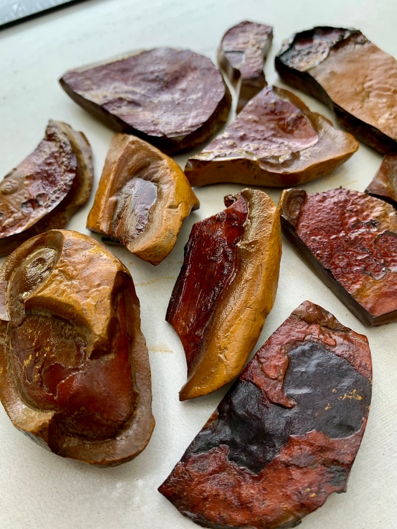May include: A collection of 10 irregularly shaped pieces of red, brown, and black jasper. The jasper is polished and has a smooth, shiny surface.
