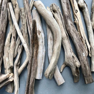 May include: A collection of driftwood sticks in various sizes and shapes, with a natural, weathered gray and brown color. The sticks are arranged in a random pattern, creating a rustic and organic aesthetic.