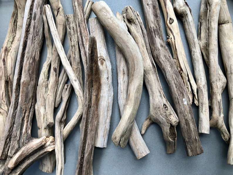 May include: A collection of driftwood sticks in various sizes and shapes, with a natural, weathered gray and brown color. The sticks are arranged in a random pattern, creating a rustic and organic aesthetic.