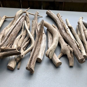 May include: A collection of driftwood branches in various sizes and shapes, with a natural, weathered gray finish. The branches are arranged in a random pattern on a gray surface.