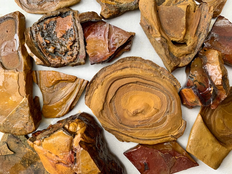 May include: A collection of brown and red agate stones with various patterns and textures. The stones are irregularly shaped and have a natural, polished finish.