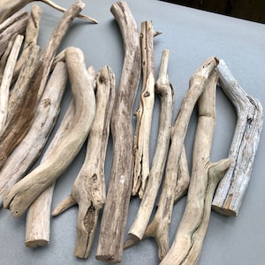 May include: A collection of driftwood branches in various sizes and shapes, with a natural, weathered finish. The branches are arranged in a loose pile on a light gray surface.
