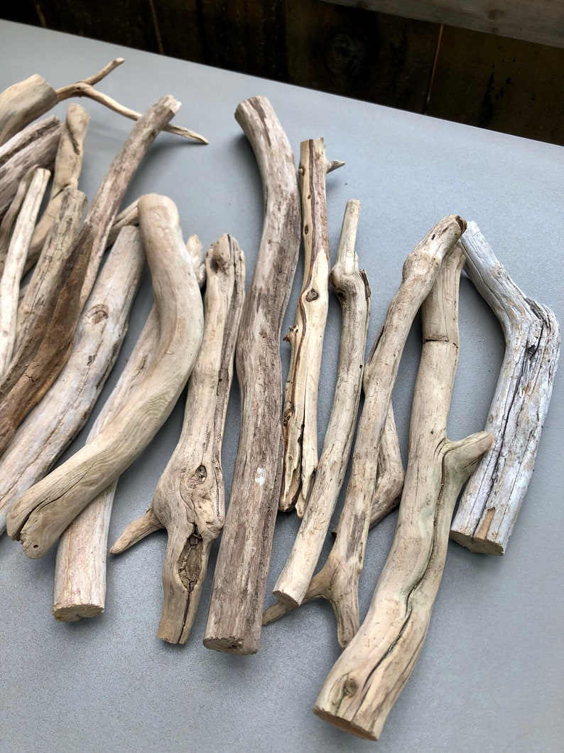 May include: A collection of driftwood branches in various sizes and shapes, with a natural, weathered finish. The branches are arranged in a loose pile on a light gray surface.