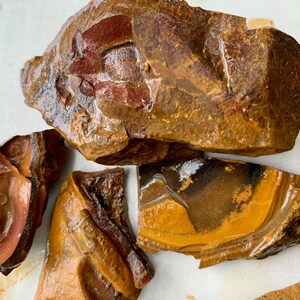 May include: Close-up of several pieces of brown, yellow, and red banded agate. The agate has a smooth, polished surface and shows natural banding patterns.