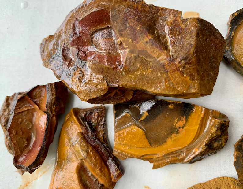 May include: Close-up of several pieces of brown, yellow, and red banded agate. The agate has a smooth, polished surface and shows natural banding patterns.