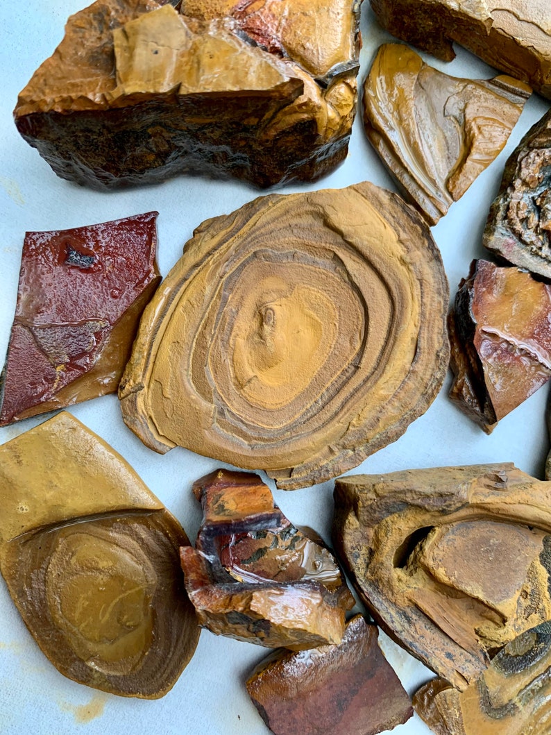 May include: A collection of polished, brown and red tiger eye stones with swirling patterns. The stones are various shapes and sizes, some with a circular pattern.