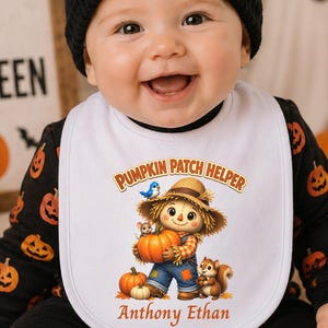 May include: A white bib featuring a graphic of a scarecrow holding a pumpkin with the text Pumpkin Patch Helper and the name Anthony Ethan, worn over a black long-sleeve shirt with an orange pumpkin pattern and a black pumpkin beanie.