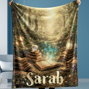 May include: A personalized blanket featuring a fantasy forest scene with stacks of books, a glowing orb, and a lantern. The name "Sarah" is displayed in a large, elegant font across the bottom. The blanket is held up by a person.