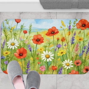 Könnte beinhalten: Eine rechteckige Badematte mit einem Aquarellgemälde einer Wildblumenwiese. Die Matte zeigt rote Mohnblumen, weiße Gänseblümchen, gelbe und violette Wildblumen und grünes Laub vor blauem Himmel und gelbem Hintergrund.